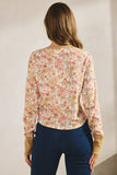 Woman wearing a floral blouse and dark pants against a plain background
